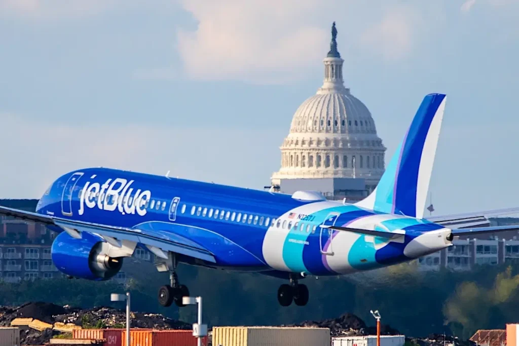 A JetBlue commercial jet approaches the runway for landing with the iconic dome of the United States Capitol building clearly visible in the distance. 05-24-25 Alexandria Virginia USA