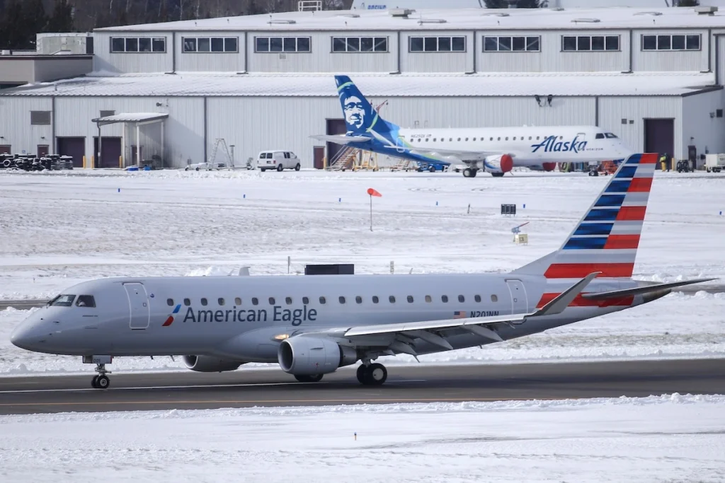 An American Eagle Embraer ERJ175 operated by Compass Airlines slowing down on the runway at Portland International Airport (PDX) on a snowy day