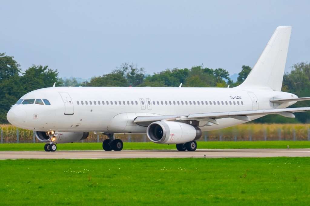 Airbus A320 on runway at regional airport preparing for takeoff with surrounding green fields and trees