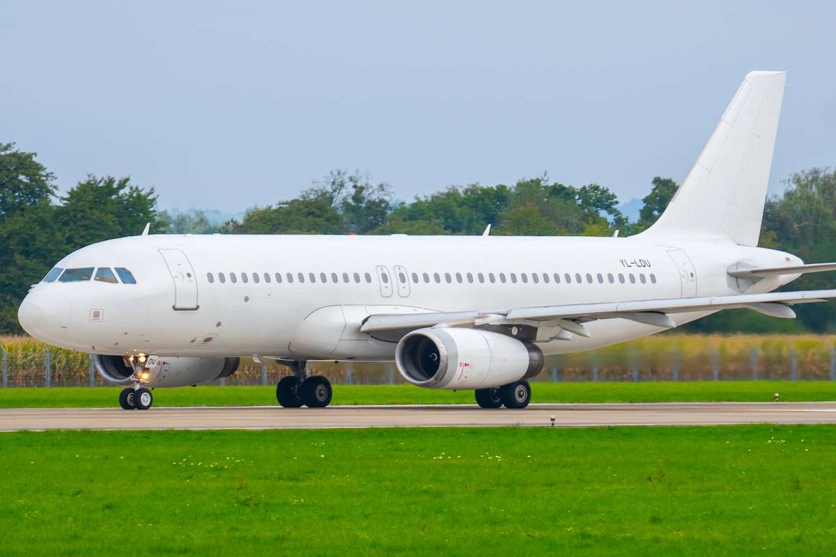 Airbus A320 on runway at regional airport preparing for takeoff with surrounding green fields and trees