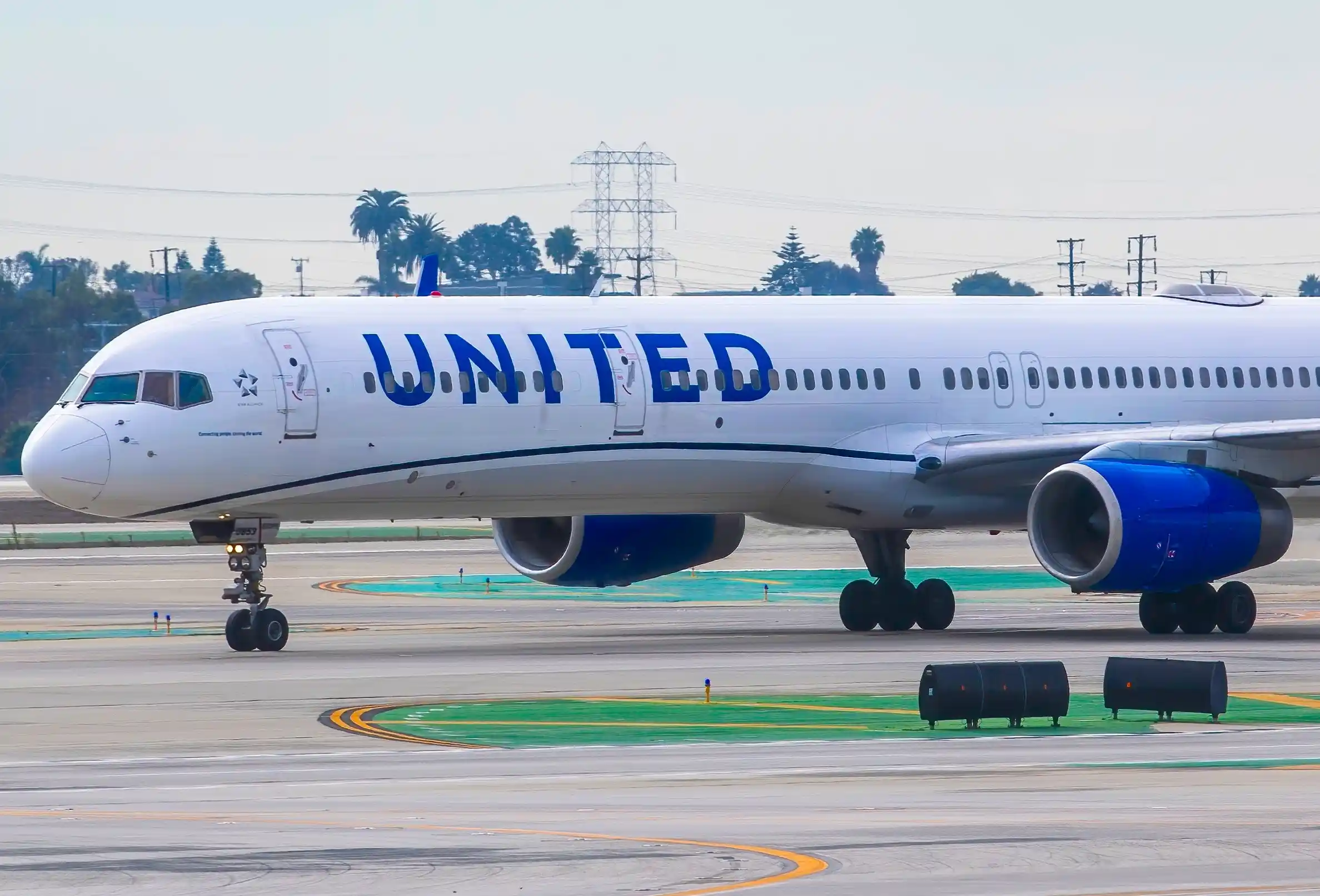United Airlines, Boeing 757-300 on the tarmac with cargo and airport vehicles in the foreground at an airport