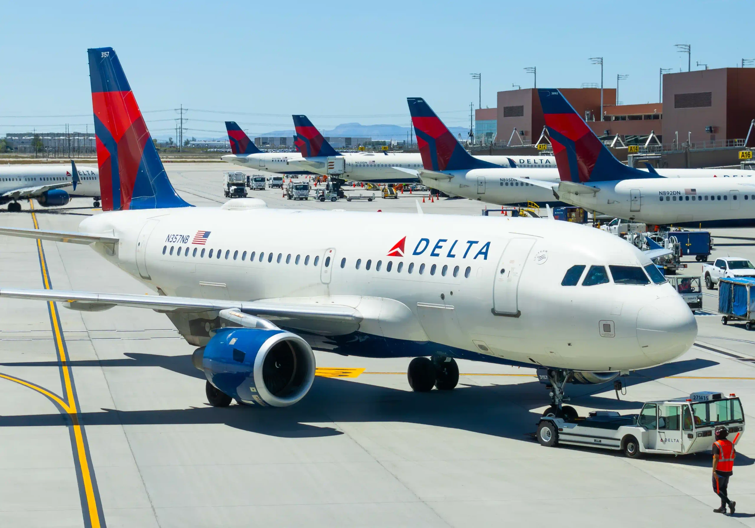 A Delta Airlines Airbus A319 pushing back from the gate at Salt Lake International Airport with multiple Delta aircraft parked behind it